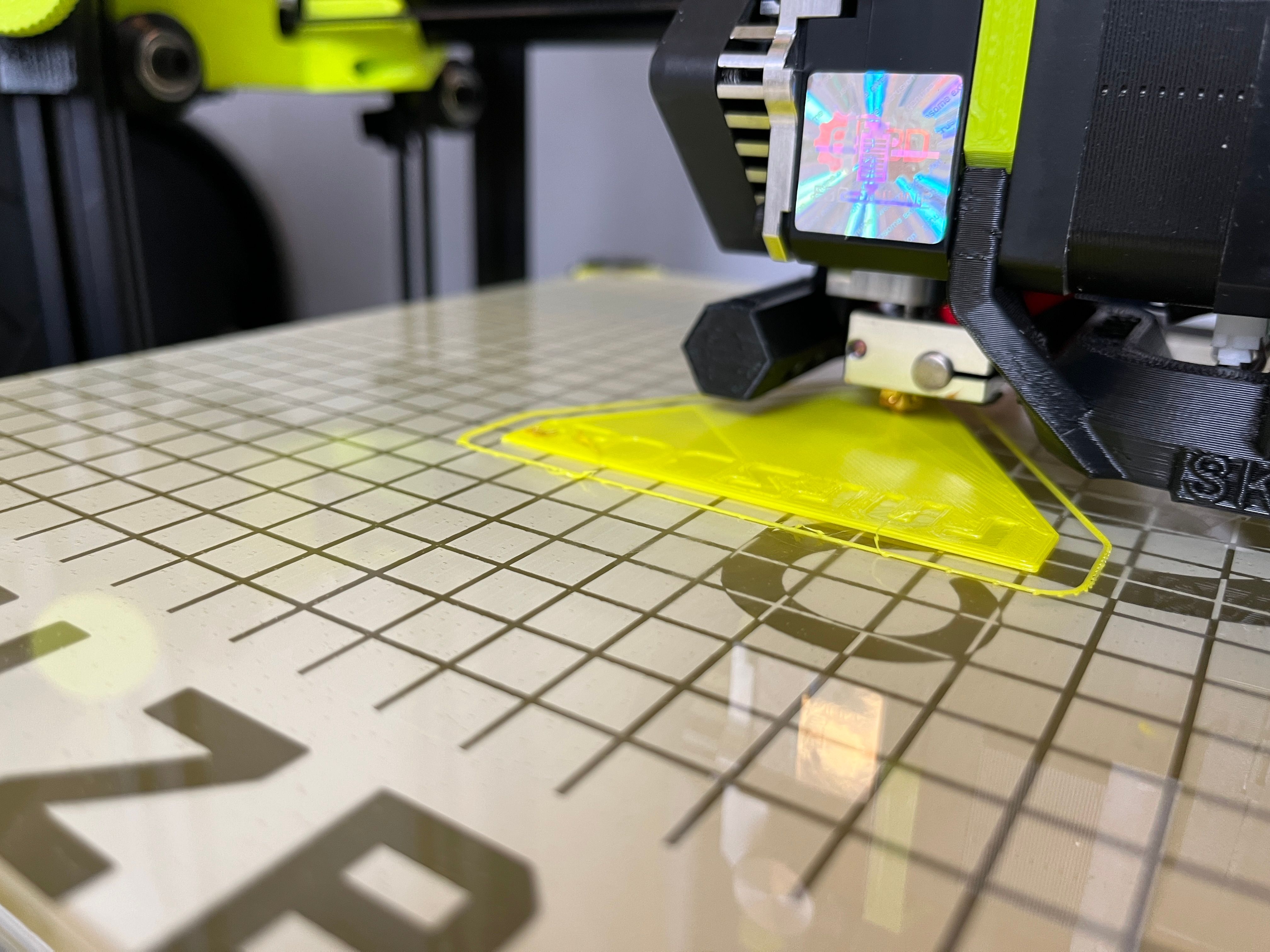 LulzBot SideKick 747 3D printing a triangular LulzBot emblem rubber stamp on a glass build surface